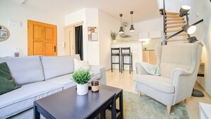 Un salon moderne comprenant un canapé, un fauteuil et une table basse, un escalier et un coin cuisine.