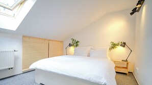 Une chambre à coucher avec un grand lit, deux tables de chevet avec des lampes, un radiateur et une fenêtre avec des stores.