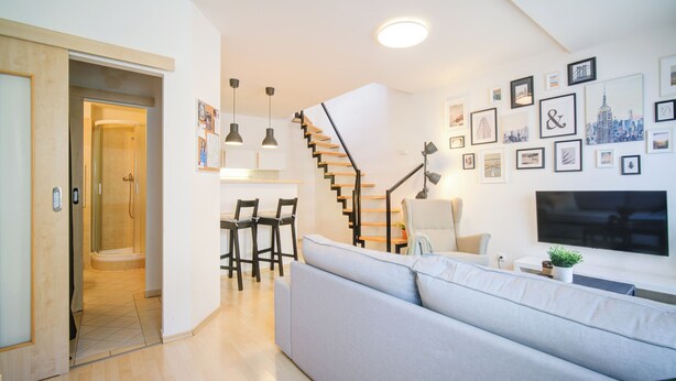 Un salon moderne avec un escalier, un canapé et un téléviseur.