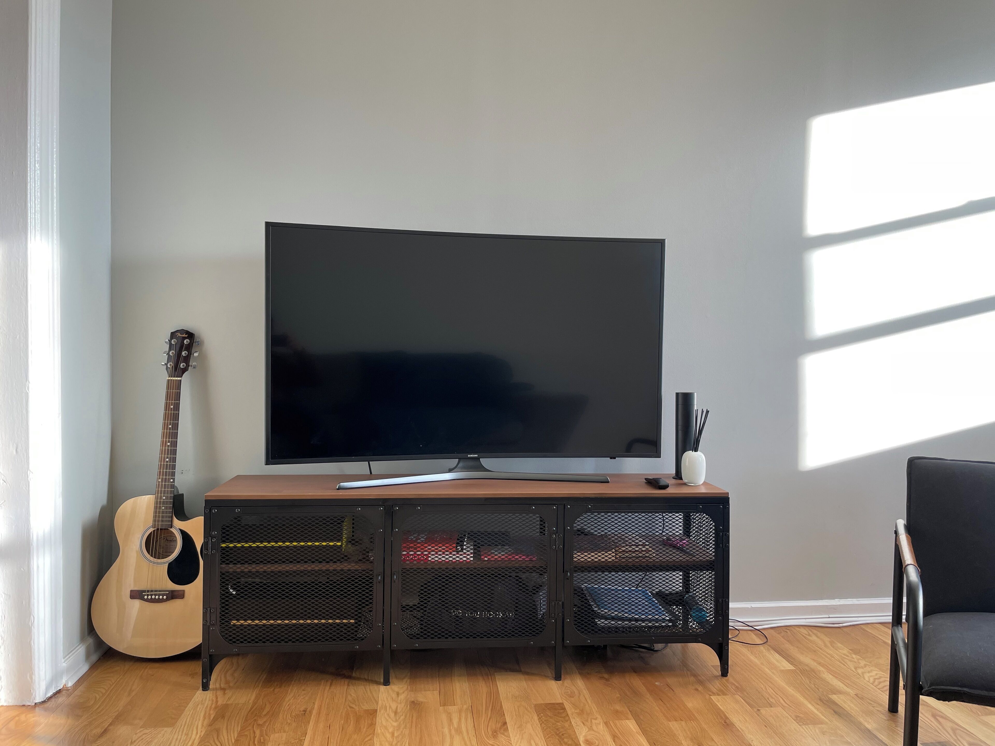 Un salon avec un téléviseur à écran plat posé sur un meuble en bois, une guitare et un fauteuil noir.