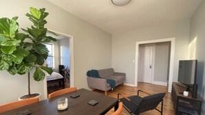 A modern living room with a dining table, chairs, a sofa, a large plant, and a television.
