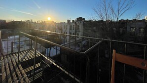 A rooftop with a metal railing, a view of buildings, and a clear sky.