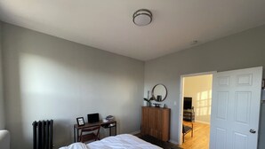 A bedroom with a bed, a desk with a laptop, a radiator, and a wardrobe.