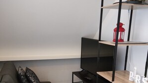A modern living room with a grey sofa, a black TV stand, and a wooden shelf with a red lantern and Eiffel Tower decoration. - Cosy house near Paris (Le Plessis-Pâté)