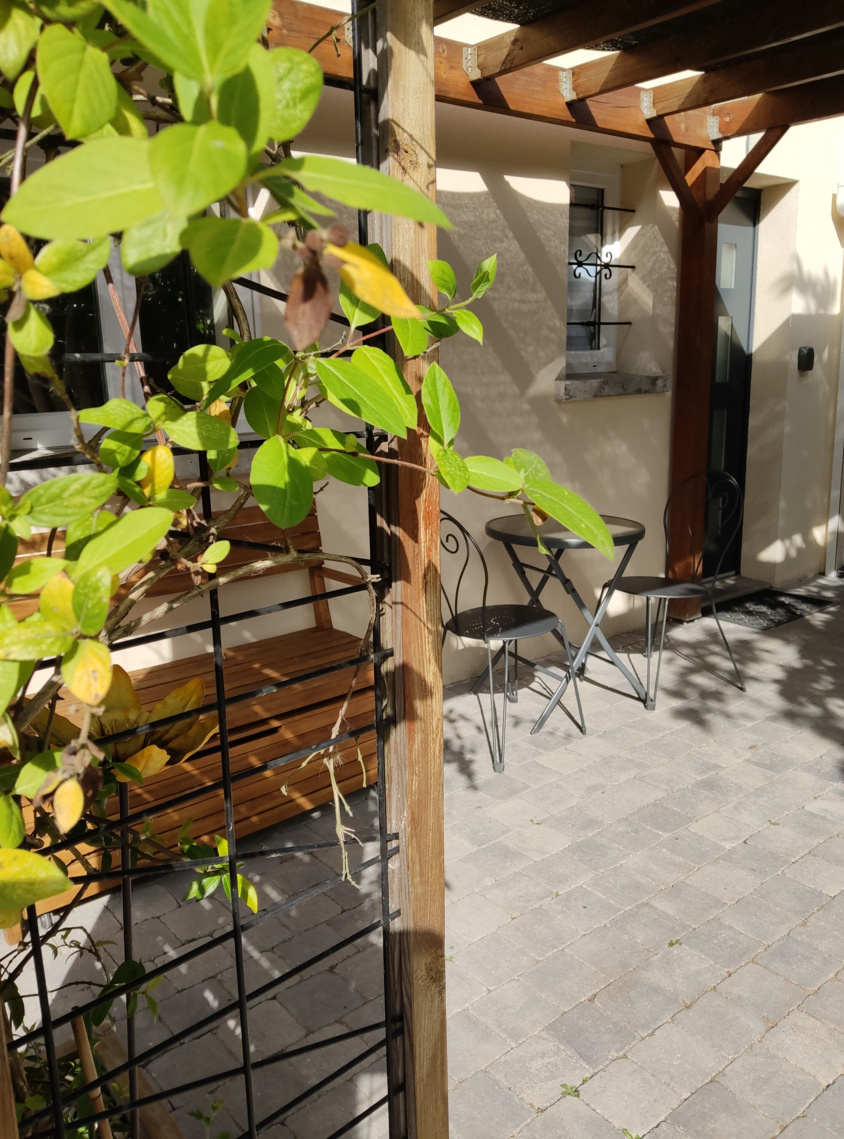 En uteplats med en pergola av trä, ett spaljé av metall och en sittgrupp bestående av ett bord och stolar.