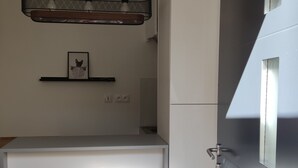 A compact kitchen with a built-in refrigerator, a hanging light fixture, and a small shelf with a framed picture. - Cosy house near Paris (Le Plessis-Pâté)