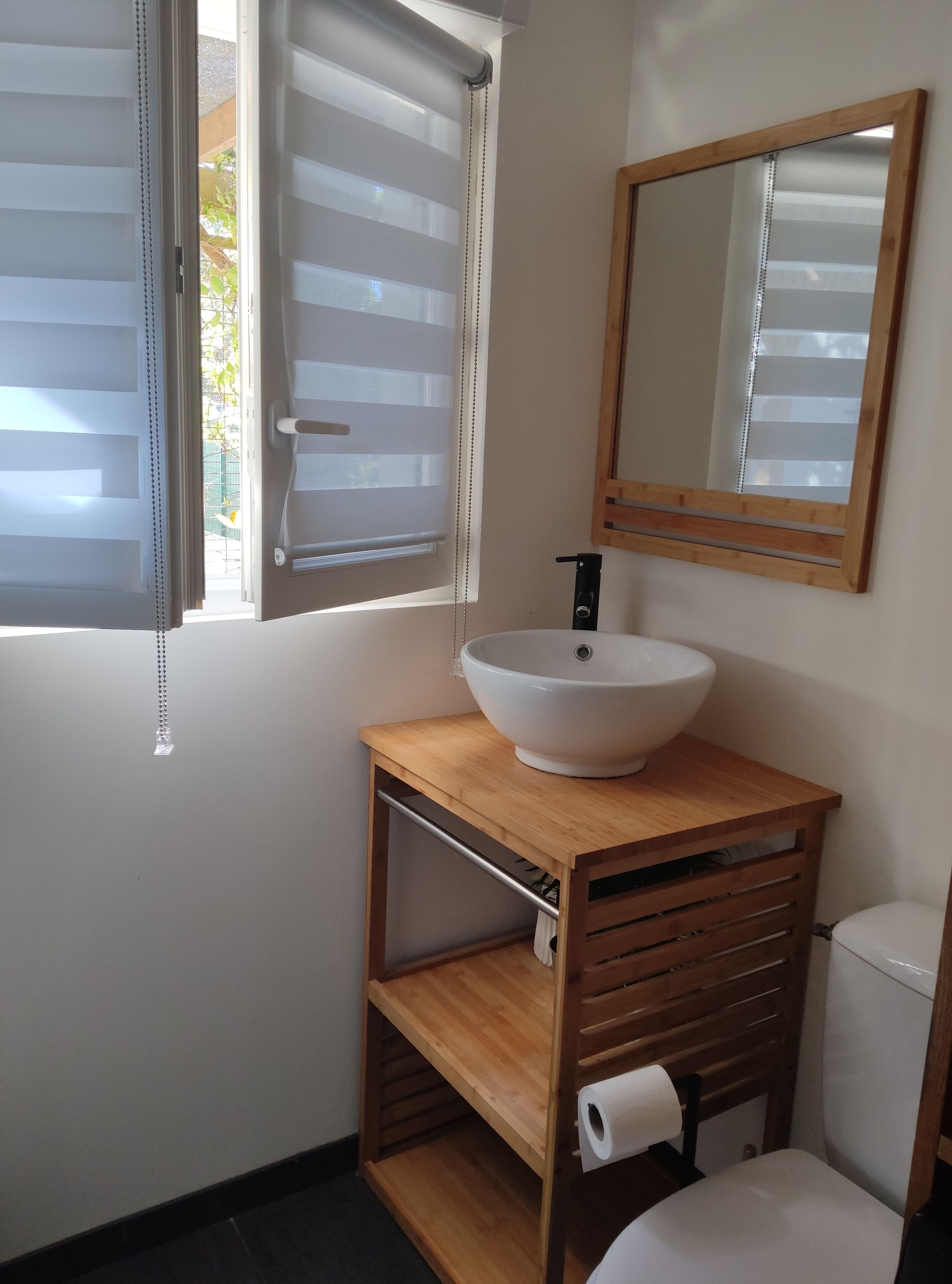 Een badkamer met een houten wastafelmeubel, een witte wasbak, een spiegel en een toilet.