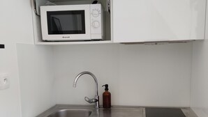 A compact kitchen with a white microwave, stainless steel sink, and a built-in stove. - Cosy house near Paris (Le Plessis-Pâté)