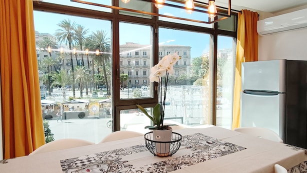 A dining area with a table set for two, a potted orchid, and a view of palm trees and buildings through large windows.