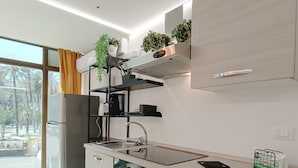 A modern kitchen with a built-in oven, a sink, and a coffee machine. There are cabinets and a countertop with a plant on the shelf.