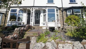 A two-story cottage with a stone facade, a front porch, and a small garden area with a bench. - Poppy Cottage (Windermere)
