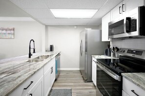 A modern kitchen with white cabinets, a stainless steel refrigerator, a microwave, and an oven. - GP32A | G. Prairie Retreat | 3BD | Pool | 2 Patios (Grand Prairie)