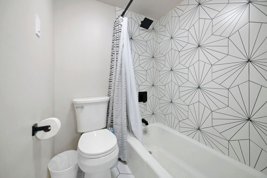 Une salle de bain avec des toilettes, une poubelle blanche, une baignoire et un rideau de douche.