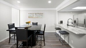 A modern kitchen with a marble countertop, stainless steel appliances, and a dining area with a dark wooden table and chairs.