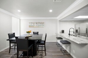 A modern kitchen with a marble countertop, stainless steel appliances, and a dining area with a dark wooden table and chairs.
