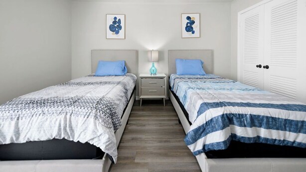 A bedroom with two beds, a nightstand, a lamp, and a door.