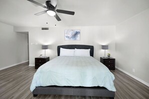 A modern bedroom with a bed, two bedside tables, a ceiling fan, and a wall-mounted artwork. - GP32A | G. Prairie Retreat | 3BD | Pool | 2 Patios (Grand Prairie)