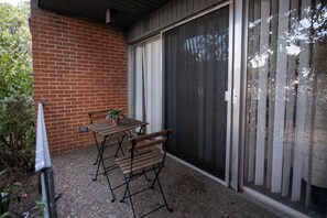 Un patio con una mesa, sillas, una planta en maceta y un ventanal corredero.