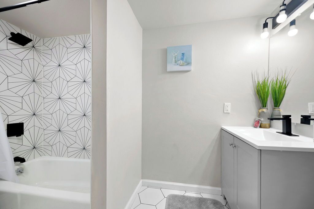 A modern bathroom with a geometric-patterned shower wall, a white sink with a black faucet, and a small potted plant.