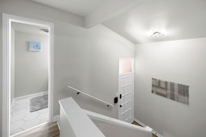 Un interior moderno con una escalera, una puerta con un pequeño ventanal y una obra de arte colgada en la pared.