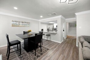 Una cocina moderna con armarios blancos, una isla central y una zona de comedor con una mesa y sillas oscuras.