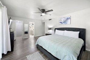 A bedroom with a bed, a ceiling fan, a painting, and a door leading to a bathroom.