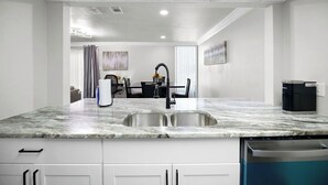 A modern kitchen with a marble countertop, stainless steel sink, and built-in dishwasher.