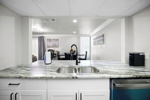 A modern kitchen with a marble countertop, stainless steel sink, and built-in dishwasher.