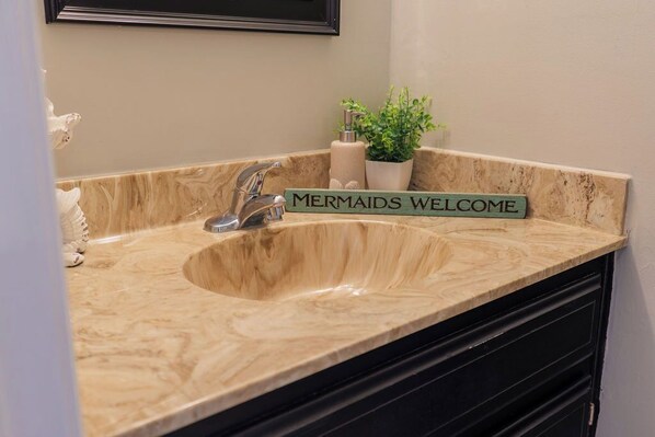 A bathroom sink with a marble countertop and a sign that reads "Mermaids Welcome". - Seas The Day with this cozy 2-bedroom lakefront condo. (Lake Park)