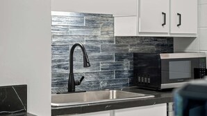 A kitchen with a stainless steel sink, black faucet, and a black microwave.