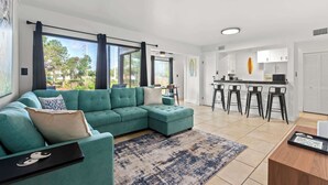 A modern living room with a teal sectional sofa, a bar area with stools, and a kitchen in the background.