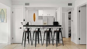 A modern kitchen with white cabinets, a black countertop, and four black bar stools.