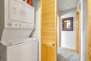 Une buanderie équipée d’un lave-linge et d’un sèche-linge à chargement frontal, d’une porte en bois et d’un miroir au mur.