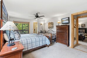 A bedroom with a bed, dresser, ceiling fan, and a television.