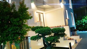 A modern building with a glass facade, a central courtyard with a bonsai tree, and a staircase leading to an upper level. - Arbnor Boutique Hotel (Tirana)