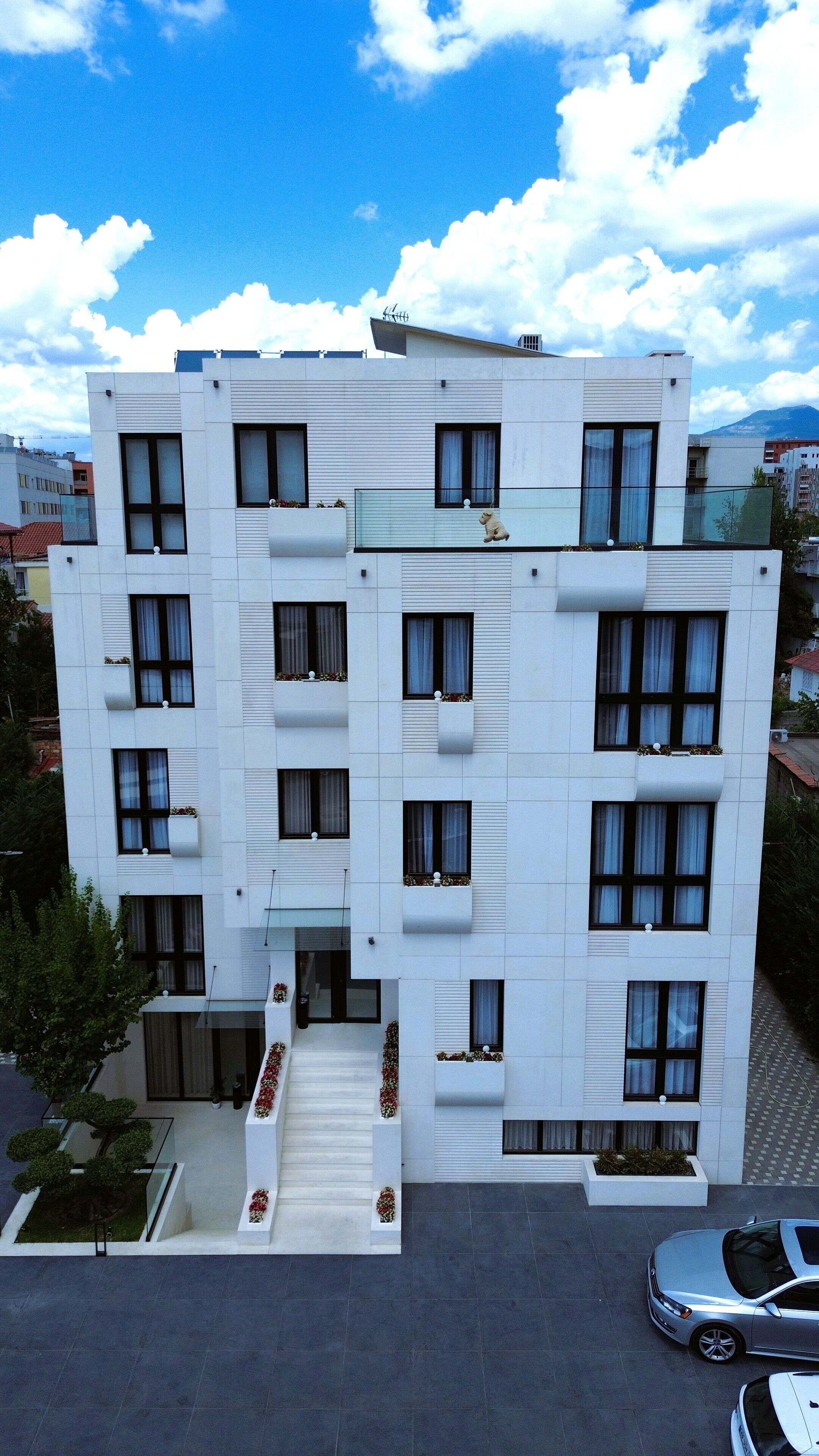 A modern multi-story building with balconies, large windows, and a parking area.