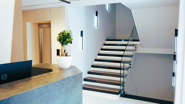 A modern reception area with a wooden desk, a potted plant, and a staircase with glass railings. - Arbnor Boutique Hotel (Tirana)
