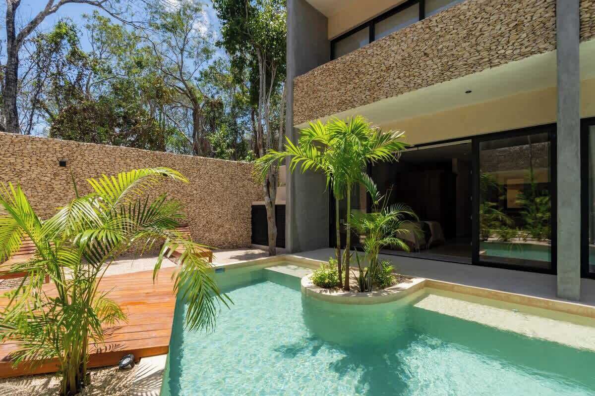 A modern outdoor pool area with a stone wall, palm trees, and a wooden deck.