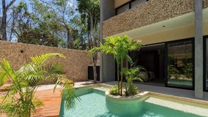 Zona de piscina moderna al aire libre con muro de piedra, palmeras y terraza de madera.