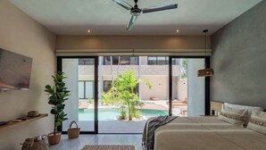 Un dormitorio moderno con una cama grande, ventilador de techo, vista a una piscina y un balcón.