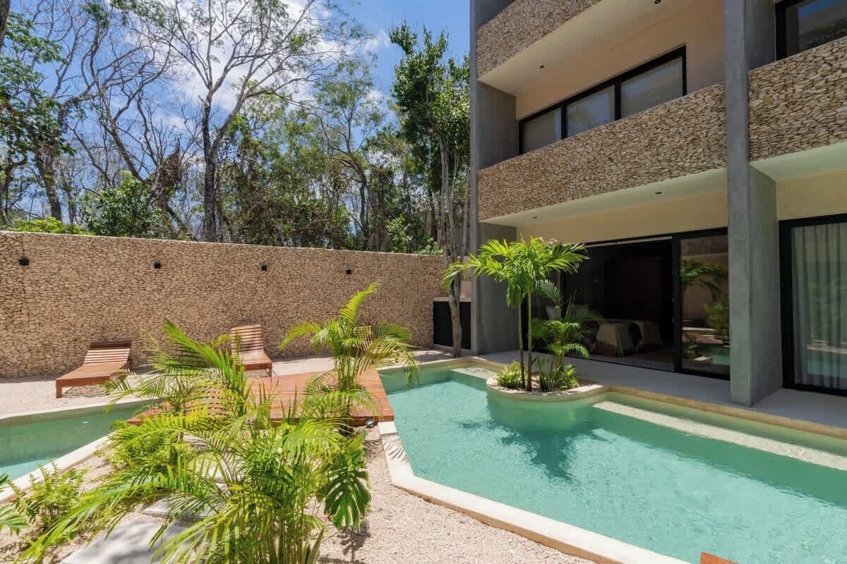 Un espace piscine extérieur moderne, doté de chaises longues, d’un mur en pierre et d’un bâtiment aux grandes fenêtres.