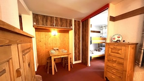 A cozy room with a wooden dining table set for four, a bunk bed with a small desk, and a dresser with a clock.