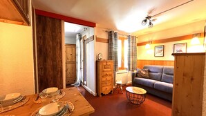 A cozy living room with a sofa, a dining table set with plates and glasses, a wooden cabinet, and a small stool.