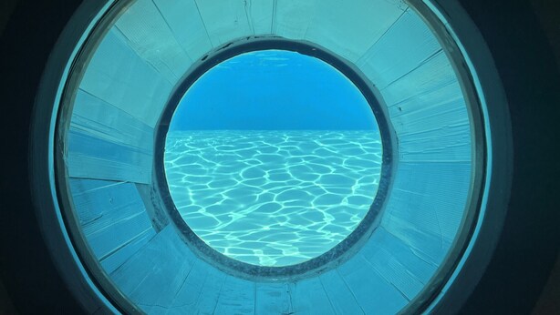 A circular window with a view of clear blue water and a blue sky.