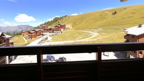 A wooden building complex with multiple balconies, a dirt road, and a mountainous backdrop. - Skis on your feet (La Plagne Tarentaise)
