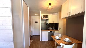 A compact kitchen with wooden flooring, white cabinets, and a dining area with a table set for two. - Skis on your feet (La Plagne Tarentaise)
