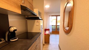 A compact kitchen with a built-in stove, a refrigerator, and a coffee machine.