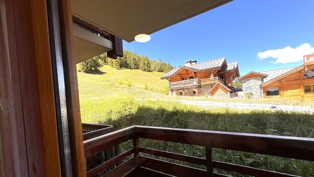 A wooden balcony with a view of a mountain lodge with stone walls and a sloped roof.