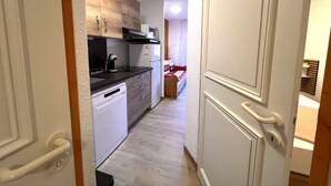 A narrow hallway leading to a kitchen with wooden cabinets, a dishwasher, and a refrigerator.