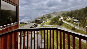 En balkon med udsigt til en vej, bygninger og en skovklædt bakke.